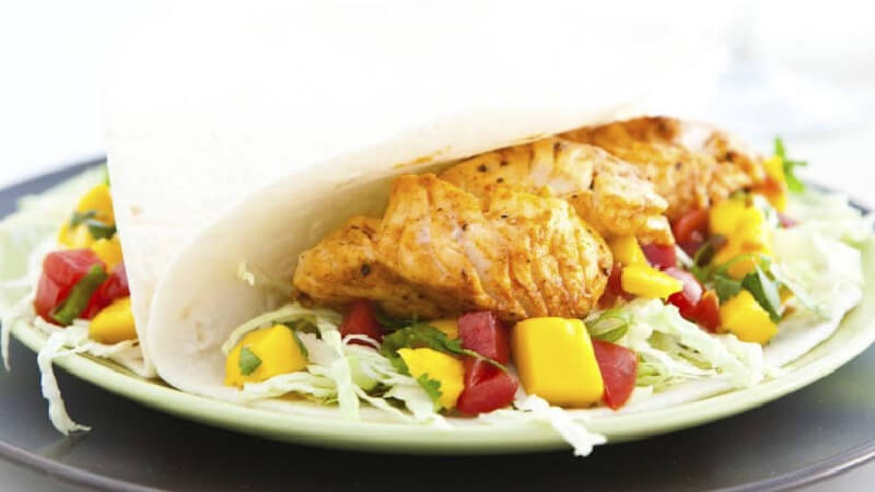 A soft taco with fish and mango salsa on a plate