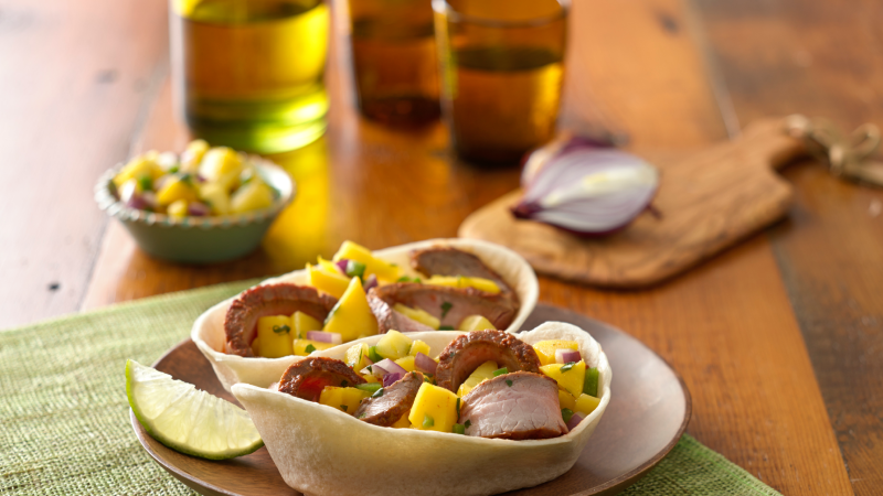 Bols de tortillas molles Old El Paso remplis de steak et de salsa à la mangue sur fond de bois.