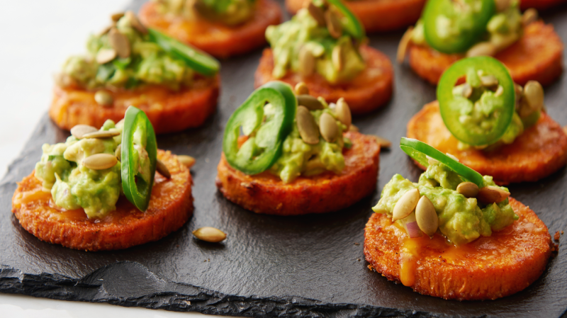 Slices of round sweet potatos with guacamole and jalapenos served on a board.