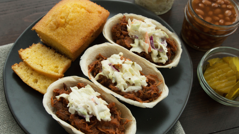 Old El Paso Mini Tortilla Bowls filled with pulled pork and slaw, served on a plate with sliced cornbread.